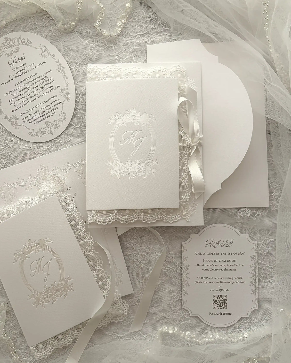 Alyson Lace White complete wedding stationery collection featuring embossed monogram details, round invitation card, ticket-style insert, coordinating envelopes arranged on delicate lace surface with tulle fabric — Polina Perri. 