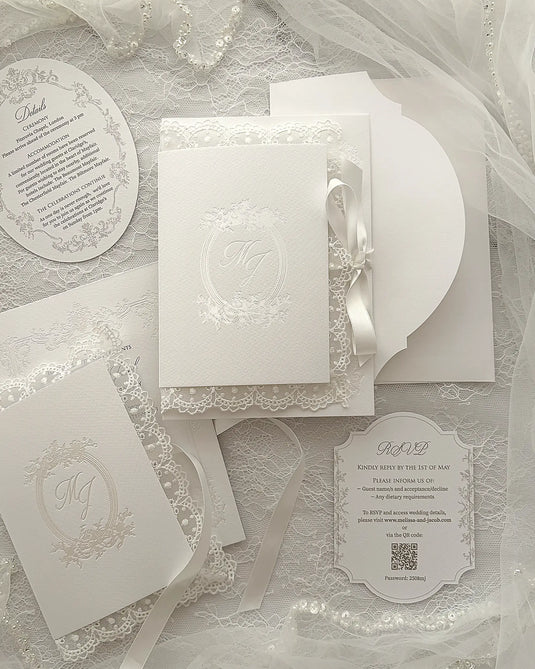 Alyson Lace White complete wedding stationery collection featuring embossed monogram details, round invitation card, ticket-style insert, coordinating envelopes arranged on delicate lace surface with tulle fabric — Polina Perri. 
