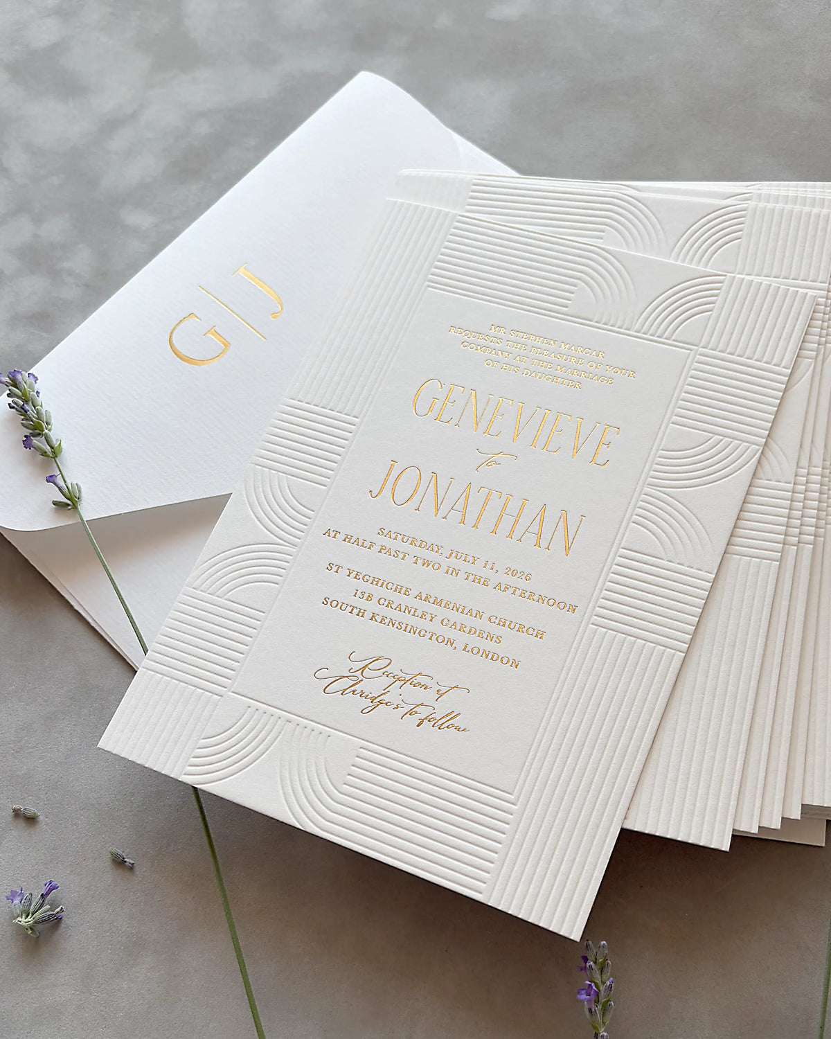 Stack of Art Deco wedding invitations with embossed wave patterns and gold foil lettering, matching envelope and dried lavender sprigs on neutral gray surface — Polina Perri