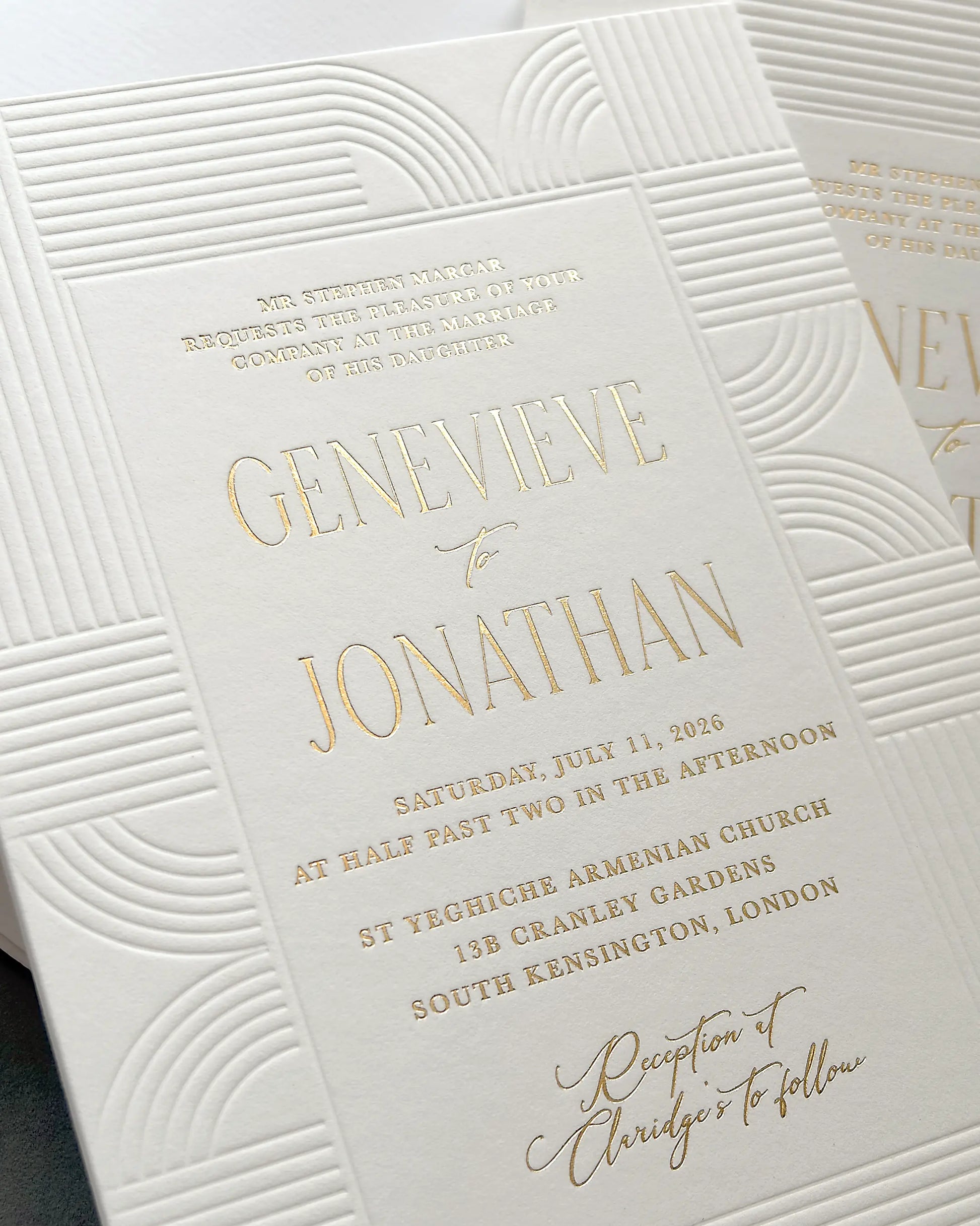 Art Deco invitation angled close-up showcasing embossed wave-pattern detail and gold foil couple's names with event information, layered composition with second card partially visible — Polina Perri