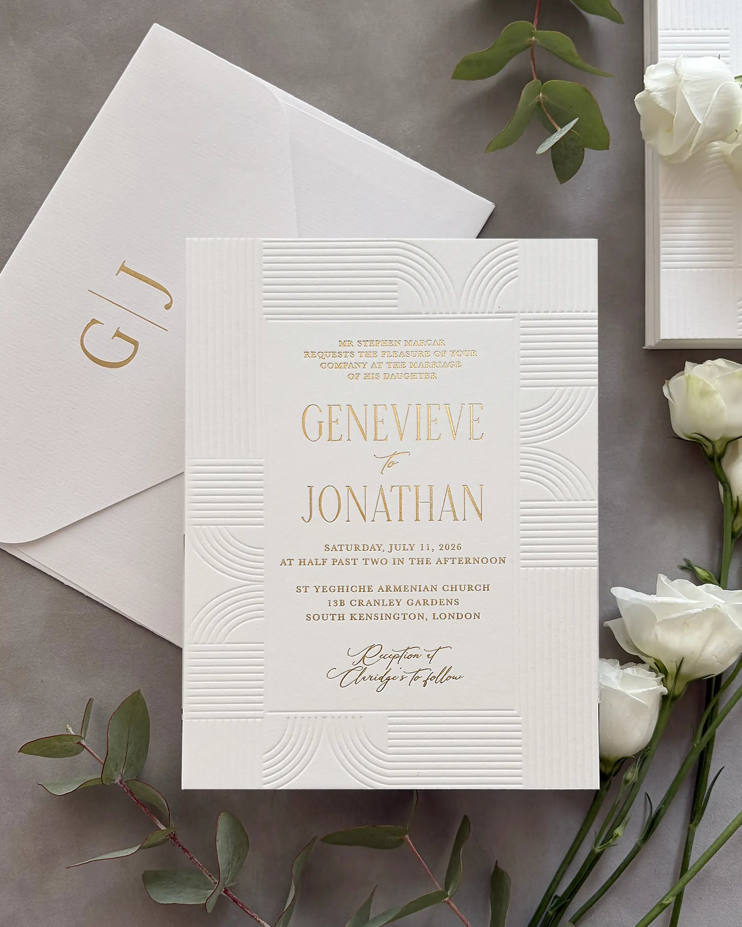 Modern Art Deco wedding invitation suite with gold foil couple's names and geometric wave-pattern design on white cotton paper, personalized envelope with gold foil monogram initials, styled with white roses and green leaves — Polina Perri. 